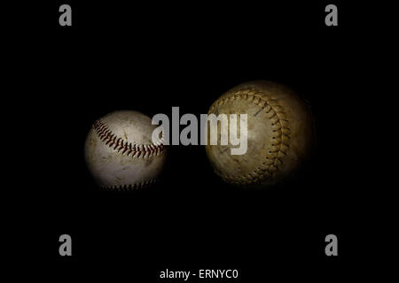 Eine abgenutzte Softball und Baseball sitzen alleine auf einem einfarbigen schwarzen Hintergrund.  Dieses Bild wurde mit einer Lightpainting-Technik beleuchtet. Stockfoto