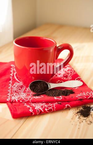 Eine rote Kaffeetasse sitzt auf einer Serviette rotes Halstuch.  Eine Kugel Kaffeesatz um verschüttet und setzt neben der Tasse. Stockfoto