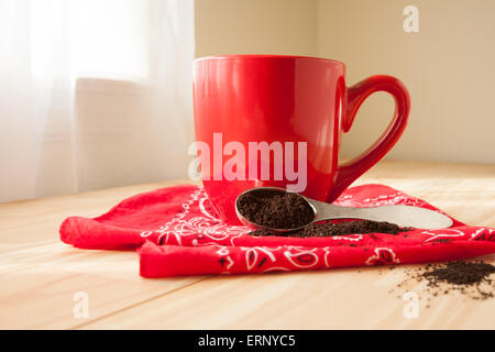 Eine rote Kaffeetasse sitzt auf einer Serviette rotes Halstuch.  Eine Kugel Kaffeesatz um verschüttet und setzt neben der Tasse. Stockfoto