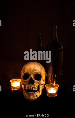 Ein Vintage Schädel sitzt neben zwei Flaschen Wein; Bild mit Kerzenlicht beleuchtet und mit einer leichten Maltechnik. Stockfoto
