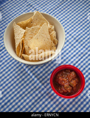 Eine Schüssel mit Mais-Tortilla-Chips setz eine rote Schale mit Salsa auf einer blau-weiß karierte Tischdecke Stockfoto