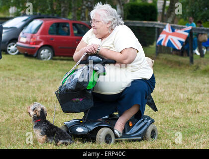 Eine größere Dame sitzt auf ihrem Elektromobil mit ihrem Haustier Hund Stockfoto