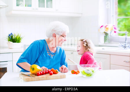 Schöne ältere Dame, glücklich liebevolle Großmutter machen gesunde Salat zum Mittagessen mit ihrer Enkelin, kleines Mädchen in der Küche Stockfoto