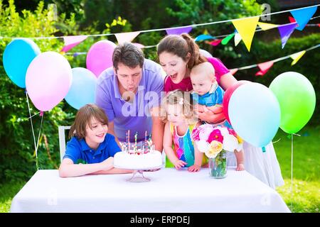 Glückliche Großfamilie mit drei kids genießen-Geburtstags-Party mit Kuchen Kerzen im Garten geschmückt mit Luftballons und Fahnen wehen Stockfoto