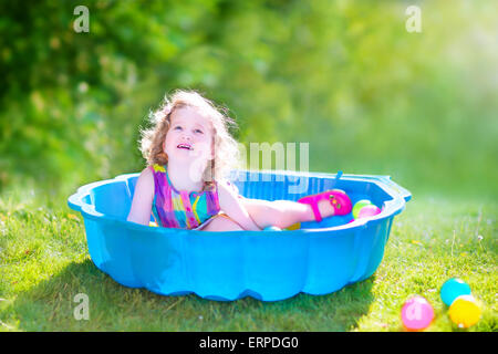 Glücklich niedlichen Kleinkind Mädchen mit dem lockigen Haar trägt eine Rosa bunt verkleiden spielen im Sandkasten mit Spielzeug aus Plastik Kugeln im Garten Stockfoto
