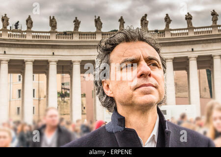 Hübscher Mann mittleren Alters, gekleidet in dunklen Mantel mit abgebrochenen Zahn, drei-Tage-Bart, Salz Pfeffer Haar und besorgten Blick während Denkmäler auf dem Hintergrund in Rom Stockfoto