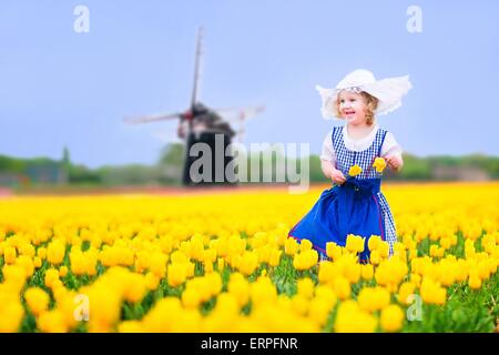 Kleinkind Mädchen tragen niederländischen nationalen Tracht Kleid und Hut spielen in einem Feld von blühenden Tulpen neben einer Windmühle Stockfoto