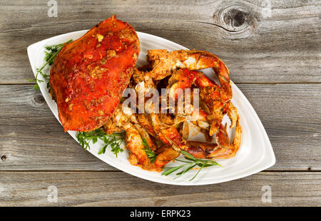 Hoher seitlicher Blick auf frisch gekochte Krabben mit pikanter Sauce und Kräutern auf weißem Teller. Rustikale Holz darunter Gericht. Stockfoto