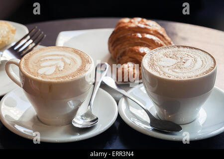 Cappuccino mit Croissant. Zwei Tassen Kaffee mit Milchschaum steht auf einem Tisch in der Cafeteria, Vintage Tonwertkorrektur Foto filt Stockfoto