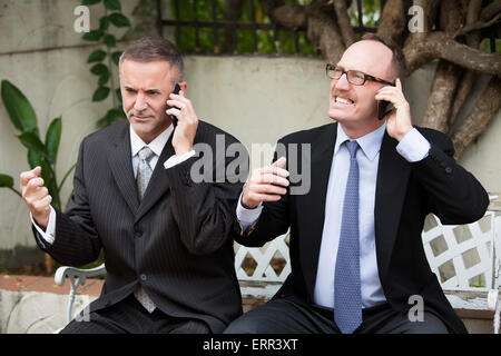 zwei Geschäftsleute draußen sitzen auf einer Bank und am Telefon sprechen Stockfoto