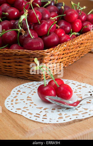 frische rote Kirschen im Korb und auf Holztisch Stockfoto