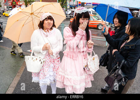 Tokio, Harajuku. Cosplay. Zwei japanische Frauen in Goth 'Sweet Lolita' Kleidung, die zwei weitere junge Frauen in schwarzer Goth-Kleidung mitnimmt. Regnen. Stockfoto