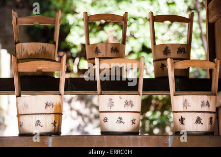 Goscha-Inari-Schrein in Kobe, Japan. Zwei Reihen mit drei Holzpfannen am Reinigungsbrunnen. Bäume außerhalb des Fokus und Licht dahinter. Stockfoto