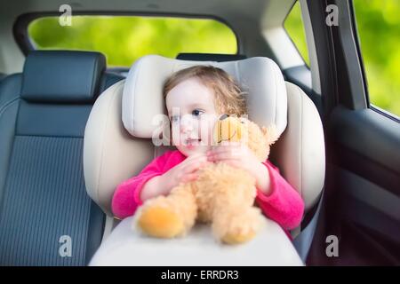 Niedliche lockige Lachen und reden Kleinkind Mädchen spielen mit einem Spielzeug-Bären genießen Sie einen Urlaub mit der Familie-Auto fahren in modernen sicheres Fahrzeug Stockfoto