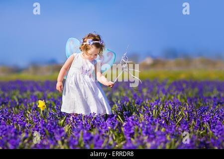 Porträt eines entzückenden Kleinkind Mädchen in eine magische Fee Kostüm und Blume Krone in ihr lockiges Haar mit einem Zauberstab im Feld spielen Stockfoto