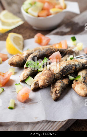 tiefe gebratene Sardinen mit Zitrone und Salat auf weißem Papier Stockfoto