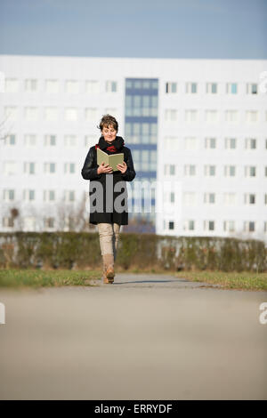 frontale Ganzkörper-Anzeigen einer reifen Frau in schwarzer Lederjacke ein Buch lesen auf die Kamera sofort Stockfoto