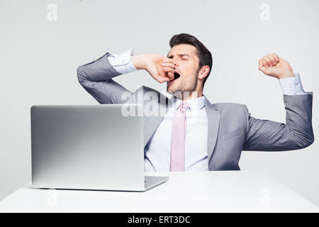 Geschäftsmann, sitzen am Tisch mit Laptop und gähnen über grauen Hintergrund Stockfoto