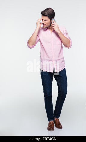 In voller Länge Portrait eines jungen Mannes reden am Telefon über grauen Hintergrund. In Hemd und Jeans tragen Stockfoto