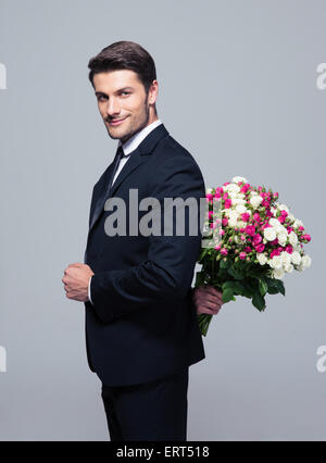 Geschäftsmann Blumenstrauß hinter seinem Rücken über grauen Hintergrund ausblenden und Blick in die Kamera Stockfoto