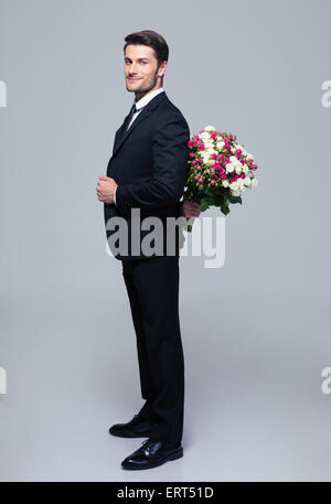 Geschäftsmann Blumenstrauß hinter seinem Rücken über grauen Hintergrund ausblenden und Blick in die Kamera Stockfoto
