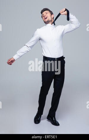 In voller Länge Portrait eines glücklichen jungen Geschäftsmann selbst mit Krawatte über grauen Hintergrund hängen Stockfoto