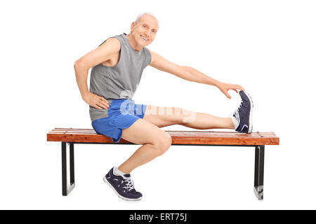 Senior in Sportbekleidung sitzt auf einer Holzbank und Dehnung Bein isoliert auf weißem Hintergrund Stockfoto