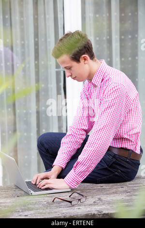 ein junger Mann in einem roten Hemd draußen zu sitzen, mit einem laptop Stockfoto