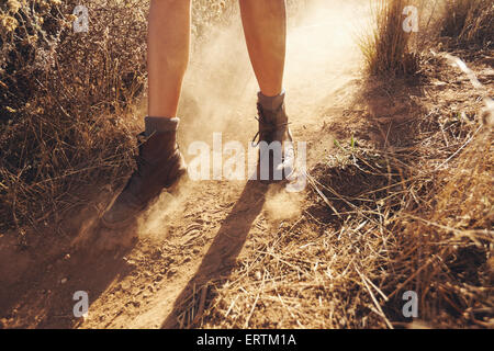 Junge Frau die Füße als She-Wanderungen auf einem Bergweg mit Staubwolke. Frau auf Feldweg in Landschaft wandern. Stockfoto