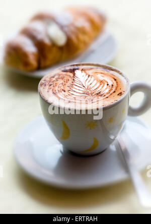 Tasse dekorative frisch gebrühten heißen Cappuccino mit einem Blattmuster im milchigen Schaum serviert mit brioche Stockfoto
