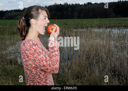 junge Frau, die an einem See einen Apfel essen Stockfoto