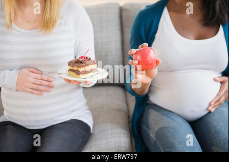 Schwangere Frauen vergleichen, Apfel und Kuchen auf sofa Stockfoto