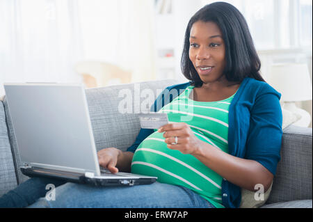 Schwarze schwangere Frau online-shopping auf sofa Stockfoto