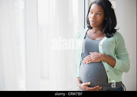 Schwarze schwangere Frau hält ihren Bauch am Fenster Stockfoto