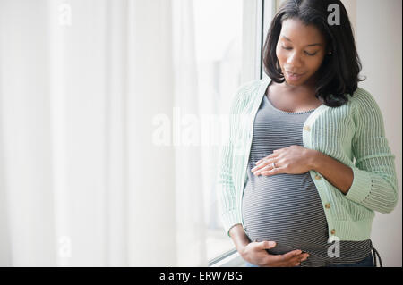 Schwarze schwangere Frau hält ihren Bauch am Fenster Stockfoto