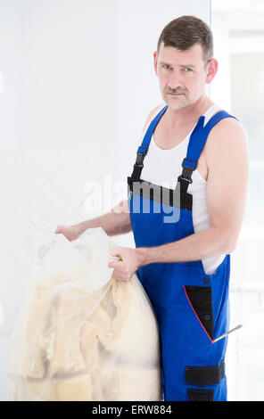 Mechaniker in einer Boilersuit ist eine Tasche von Schutt zu heben Stockfoto