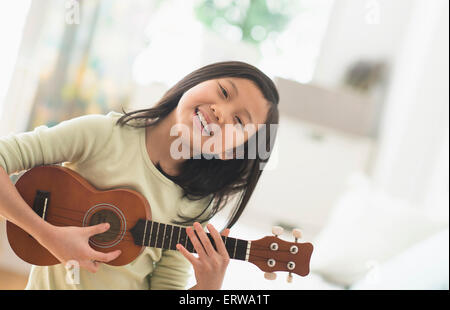 Chinesisches Mädchen üben Ukulele im Schlafzimmer