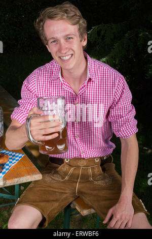 Bayerische Jüngling sitzt auf einer Bank mit einem Bierkrug in der hand Stockfoto