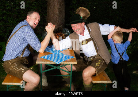 zwei bayerische Männer sitzen auf einer Bank und Pressen Hände, während ein Kind neben ihnen steht Stockfoto