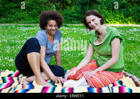 zwei Frauen sitzen auf Decke im Park mit einem Buch Stockfoto