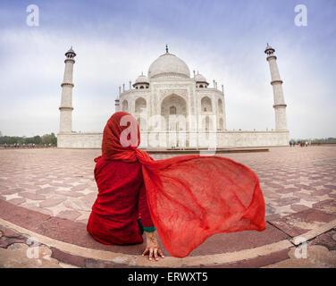 Frau im roten Kostüm mit schmeichelnden Schal sitzt in der Nähe von Taj Mahal in Agra, Uttar Pradesh, Indien Stockfoto