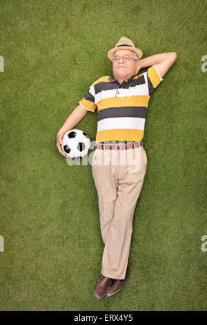 In voller Länge Portrait von einem reifen Mann auf dem Rasen liegen und halten einen Fußball neben ihm Stockfoto