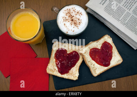 ein romantisches zubereitetes Frühstück mit Toast mit Butter und Marmelade in Form eines Herzens und einer Kaffee-Nexto ein Newpaper und eine Serviette Stockfoto