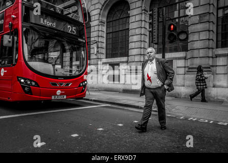 Ein Kaukasier mit Anzug und eine Krawatte mit englischer Flagge überqueren die Straße vor einem roten Doppeldeckerbus, London, Großbritannien. Stockfoto