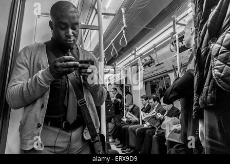 Schwarzer Mann mit seinem Handy auf einer Londoner u-Bahn. Stockfoto