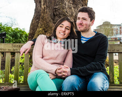 Porträt von schönen jungen Ehepaar sitzt auf einer Bank in einem Park Stockfoto