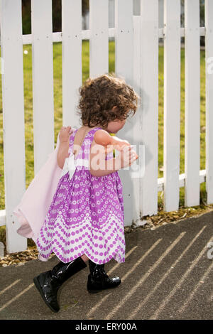 kleines Mädchen im rosa Kleid zu Fuß entlang eines weißen Zauns mit seiner Puppe Stockfoto