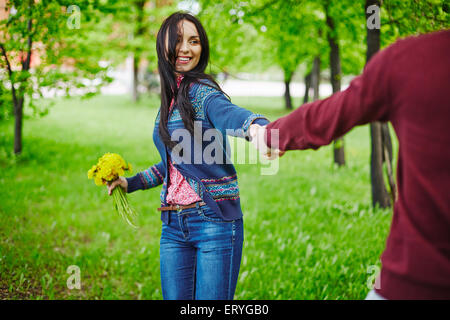 Lächelndes Mädchen mit Bündel gelber Löwenzahn hält ihren Freund mit der Hand im park Stockfoto