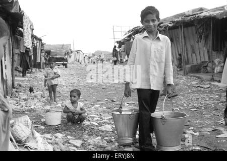 Jungen tragen zwei Eimer Wasser in Malvani Slum; Malad; Bombay Mumbai; Maharashtra; Indien nicht Herr Stockfoto