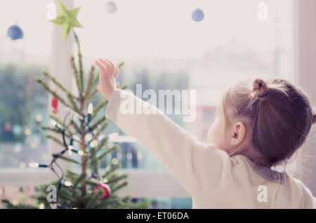Mädchen für Start am Weihnachtsbaum zu erreichen Stockfoto